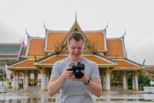 Photography Young happy tourist man checking camera against view of the Buddhist temple in B