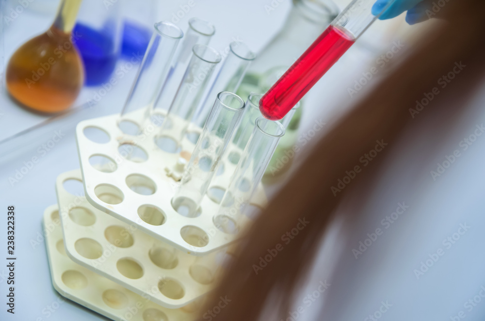 A man's hand hold and lean a glass test tube(Proberohr) with red(magenta) water(liquid, fluid) on the reflected desk in the laboratory A man's hand hold and lean a glass test tube(Proberohr) with red(magenta) water(liquid, fluid) on the reflected desk in the laboratory