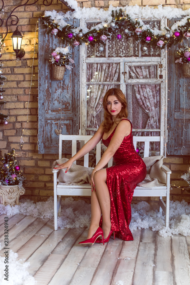 Fototapeta premium Winter holidays, celebration and people concept - young sexy woman in elegant red dress over christmas interior background