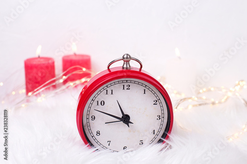 Red clock - symbol of New Year and birning candles on white fur background.