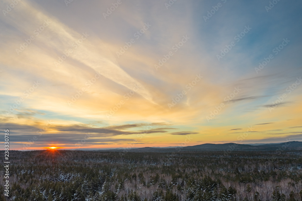 Aeria; drone panoramic view of early winter sunset, mixed forest of birches and pine trees, mountains on the background, colored dramatic sky with beautiful clouds, South Ural, Russia