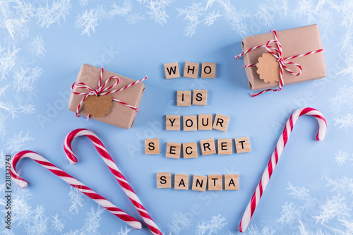Secret Santa christmas game. Wrapped gift boxes with notes candy cane on blue pastel background top view copyspace. Text from letters Who is your Secret Santa