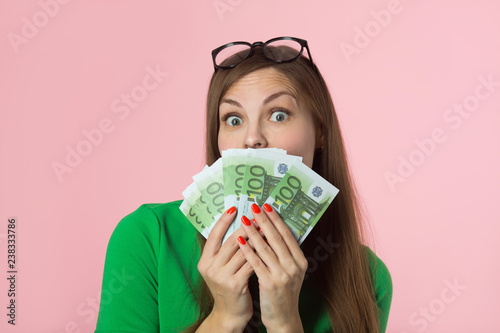 beautiful young girl holding euros and on a pink background with a surprised face