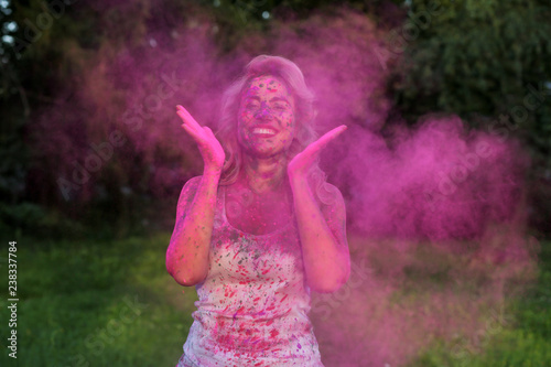 Portrait of positive young model having fun with a cloud of pink dry Holi paint at the park