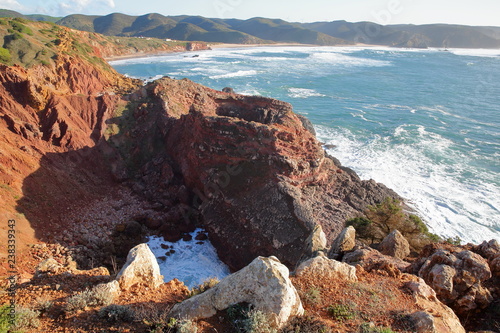 The rocky and colorful coast near Carrapateira with Amado beach in the background and strong waves, Costa Vicentina, Algarve, Portugal