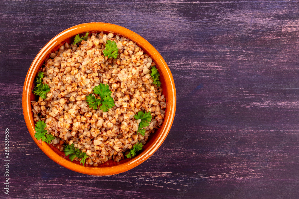 Buckwheat in a rustic earthenware bowl, garnished with fresh parsley leaves, shot from the top on a dark wooden background with a place for text Buckwheat in a rustic earthenware bowl, garnished with fresh parsley leaves, shot from the top on a dark wooden background with a place for text