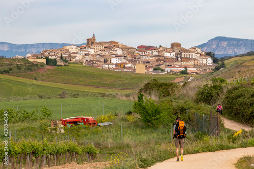 Rear view of two pilgrims on the Way of St. James, Camino de Santiago in Spain, the Cirauqui or Zirauki urban skyline in the distance photo
