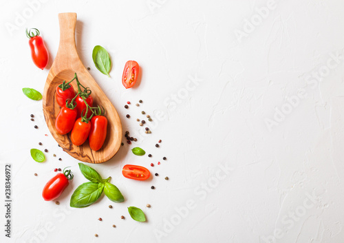 Organic Mini San Marzano Tomatoes on the Vine with basil and pepper in oilve wood plate on white kitchen background. Space for text