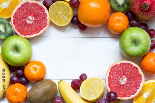 Fruit frame background with oranges  tangerines  banana  apple  lemon on white wooden table  healthy food frame