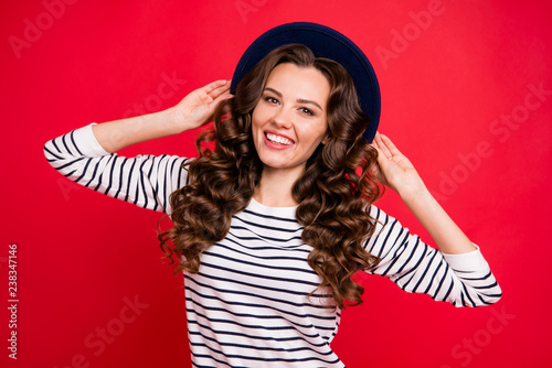 Portrait of nice sweet lovely attractive pretty cheerful positive cheery wavy-haired lady wearing striped pullover touching sunhat isolated over bright vivid shine red background
