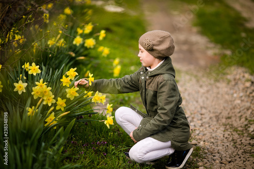 Cute happy little girl in the spring country smelling yellow daffodils © Lena May