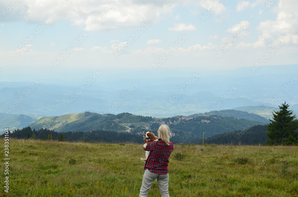 Woman holding her dog and watching picturesque mountain landscape