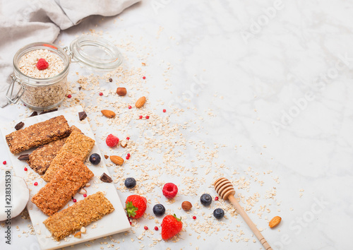 Organic cereal granola bar with berries on marble board with honey spoon and jar of oats and linen towel on marble background. Space for text.Top view photo