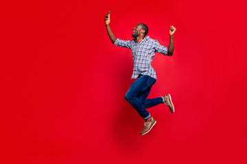 Full length body size profile side view of nice funny crazy handsome cheerful guy wearing checkered shirt holding in hands cell reading text going in air isolated on bright vivid shine red background