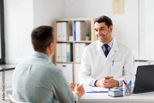 medicine, healthcare and people concept - smiling doctor talking to male patient at medical office in hospital