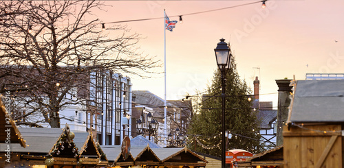 Christmas Market and tree. Stalls decorated with lights. British flag on sunset sky.