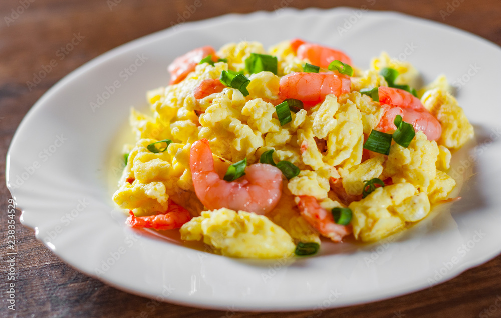 scrambled eggs with shrimp and green onions in white plate on wooden table background. scrambled eggs with shrimp and green onions in white plate on wooden table background.