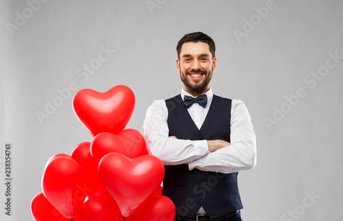 valentines day, love and people concept - happy man with red heart shaped balloons over grey background