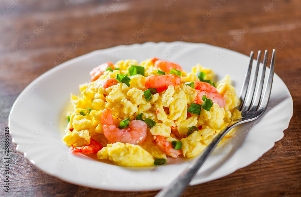 scrambled eggs with shrimp and green onions in white plate on wooden table background.