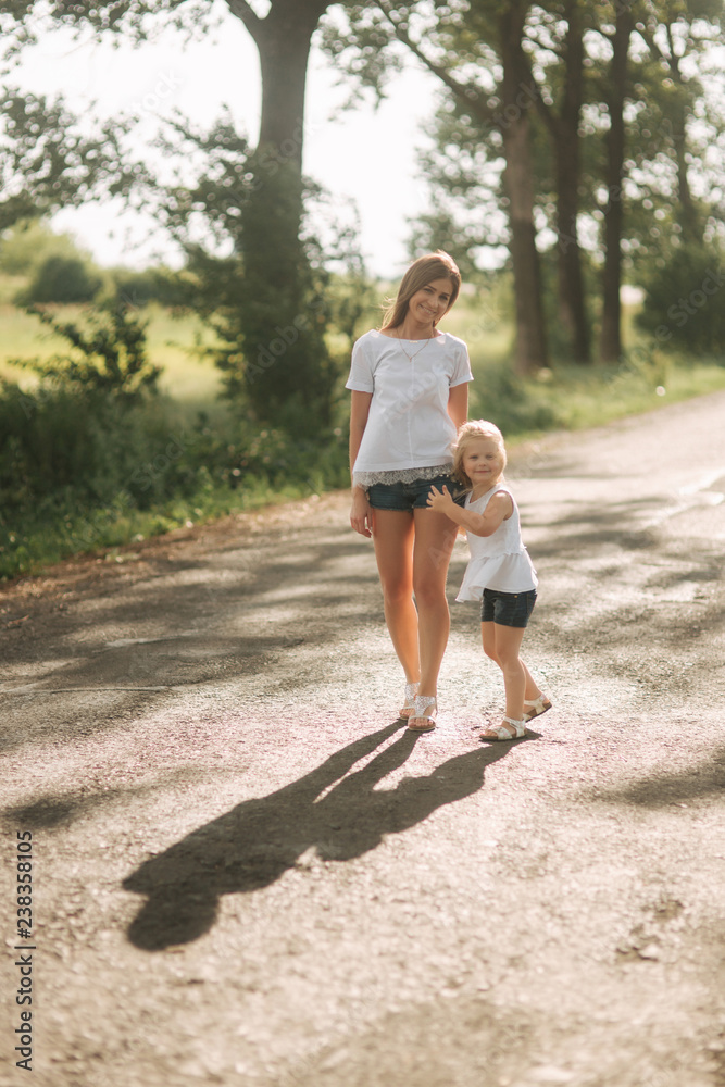 Mother and little daughter walk though the alley and hold each others hands. Shadow on the road Mother and little daughter walk though the alley and hold each others hands. Shadow on the road