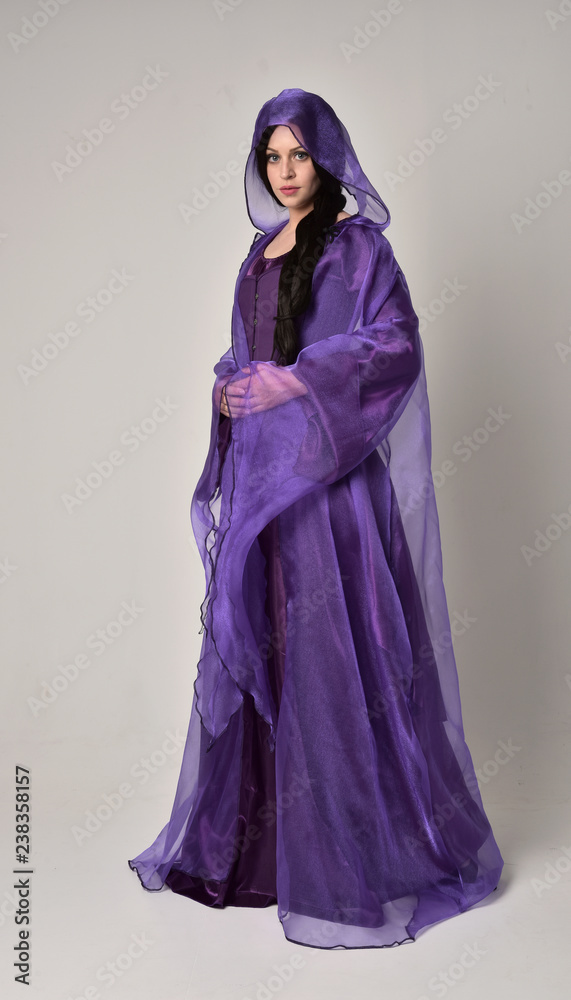 full length portrait of beautiful girl with long black hair, wearing purple fantasy medieval gown and cloak. standing pose on grey studio background. full length portrait of beautiful girl with long black hair, wearing purple fantasy medieval gown and cloak. standing pose on grey studio background.