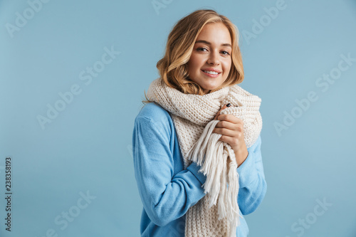 Image of blond woman 20s wrapped in scarf smiling at camera, isolated over blue background