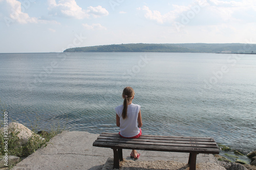 girl looks at the sea sitting on a bench on the beach