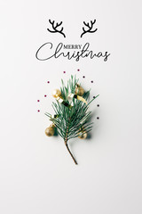 top view of little pine tree branch with ribbon and christmas balls on white surface with "merry christmas" lettering with deer horns