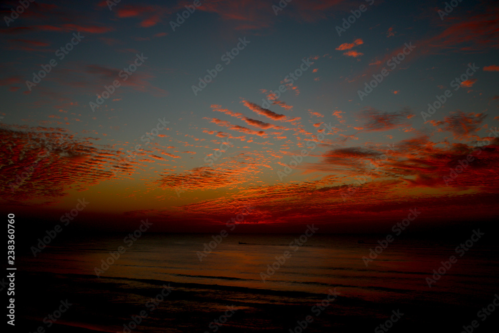 sunset at sea, red sun sits behind the horizon