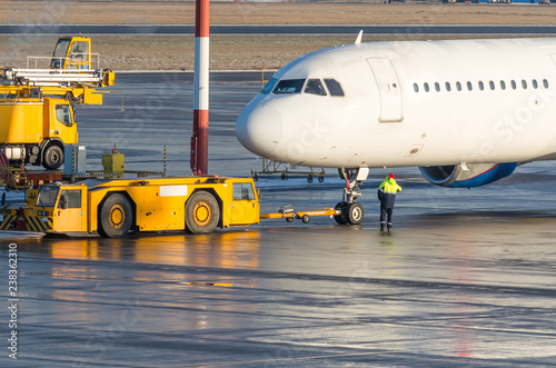 The pushback tractor is towing the aircraft to a parking lot, aviation marshall.