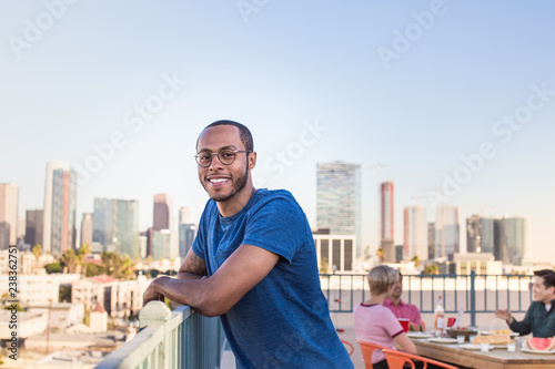 Portrait of young adult male at a rooftop party with city skyline