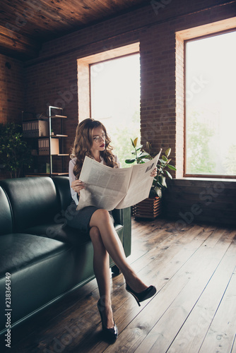 Nice stylish classy chic attractive stylish lady business shark sitting on divan reading morning daily newspaper routine long legs work place station loft interior