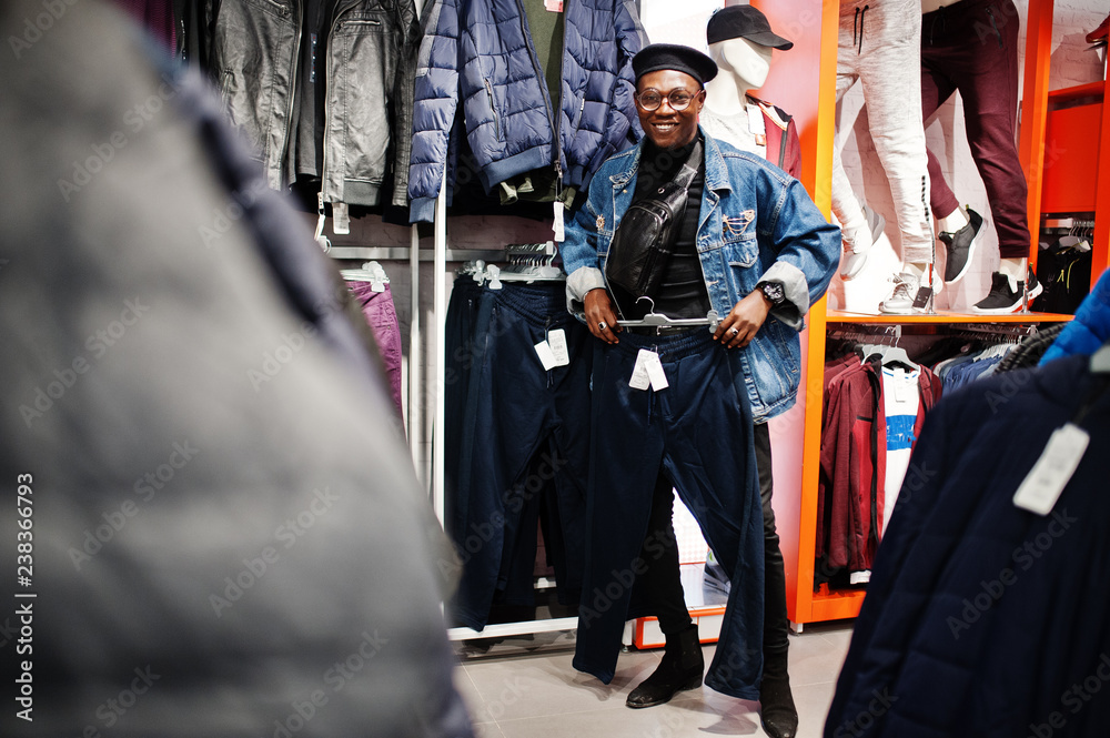 Stylish casual african american man at jeans jacket and black beret at clothes store looking on new sport pants.