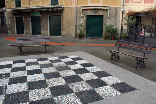 Selciato a scacchi con due panchine  e facciata con serrande