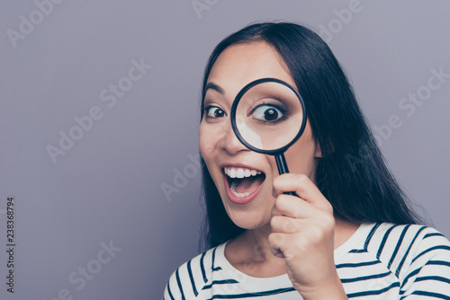 Close-up portrait of nice cool attractive funky cheerful positive straight-haired lady in striped pullover holding looking through loupe opened mouth isolated on gray pastel background