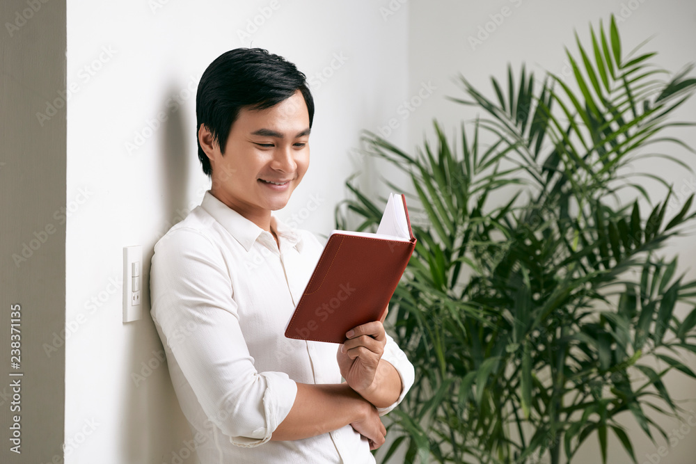 Smiling Asian manager standing with opened notepad and reading his plans for the working week Smiling Asian manager standing with opened notepad and reading his plans for the working week