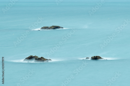 Long exposure of three rocks in the light blue sea