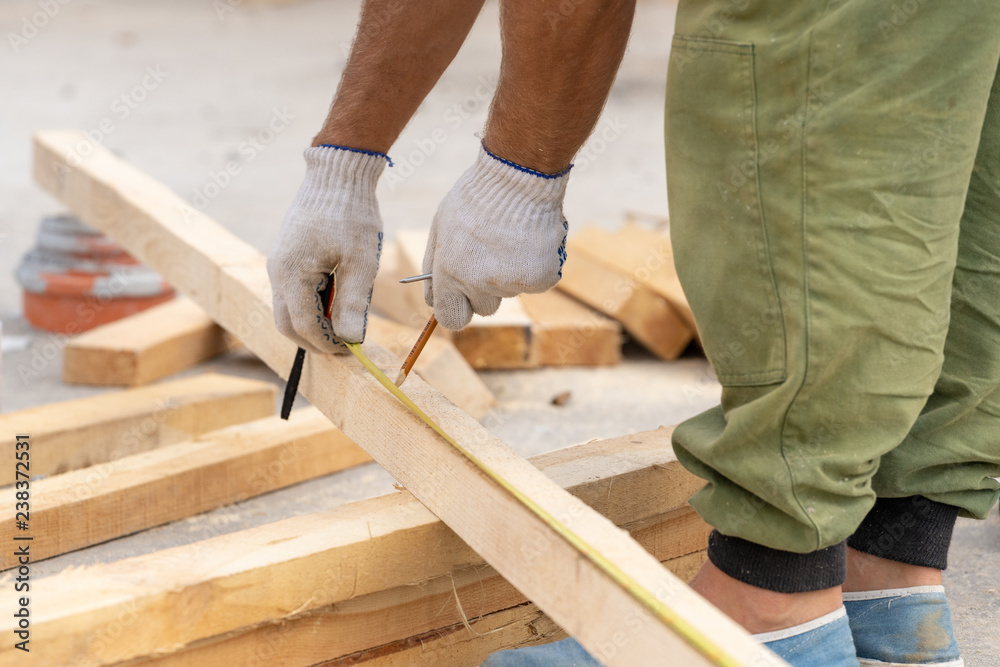 Close up cropped photo of unrecognizable man in white protective gloves on hand holding pencil making mark on plank board using measurement Close up cropped photo of unrecognizable man in white protective gloves on hand holding pencil making mark on plank board using measurement