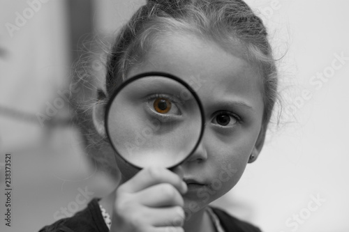  black and white creative portrait of a five-year-old girl who carefully looks at a magnifying glass