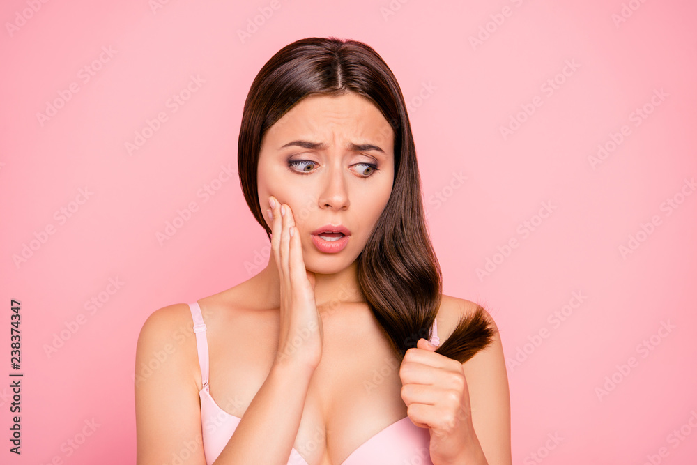 Close-up portrait of nice lovely charming attractive worried girl in beige bra holding in hand unhealthy damaged weak straight hair curls ends trouble isolated over pink pastel background Close-up portrait of nice lovely charming attractive worried girl in beige bra holding in hand unhealthy damaged weak straight hair curls ends trouble isolated over pink pastel background