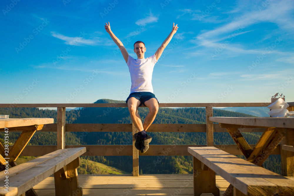 Fototapeta premium Young man sits in open air cafe with terrace and enjoy beautiful view of mountains