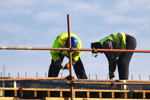 Two Workers knitting metal rods bars into framework reinforcement