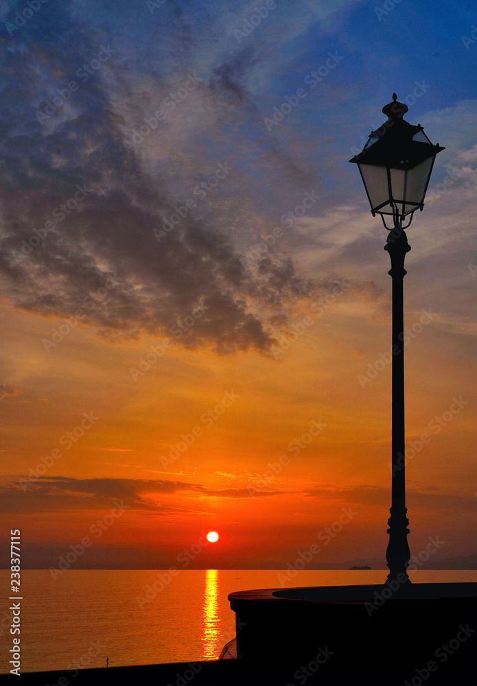 Beautiful colorful warm sunset on the beach of small italian coastal town Camogli with silhouette of old street lamp, Liguria Italy