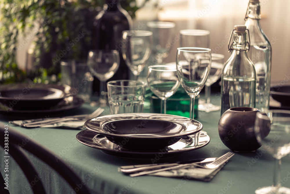 Fototapeta premium Closeup of elegant dining table with green tablecloth, black plates and wine glasses