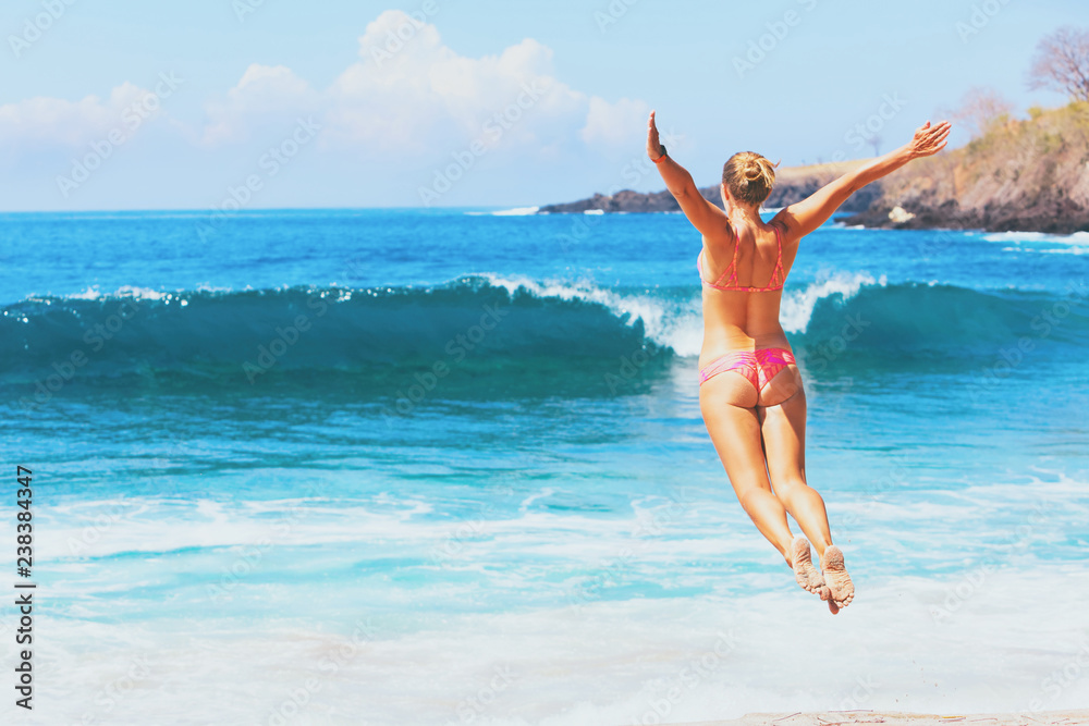 Happy family vacation. Girl in bikini jump high with spreading hand into mid air above water pool and breaking sea surf. Travel adventure lifestyle on summer beach holiday with kids on tropical island