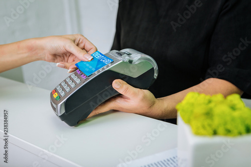 Worker of beauty salon holding pin pad while client paying by card photo