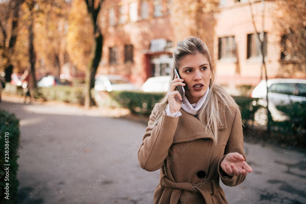 Obraz premium Serious young woman talking on the mobile phone outdoors.