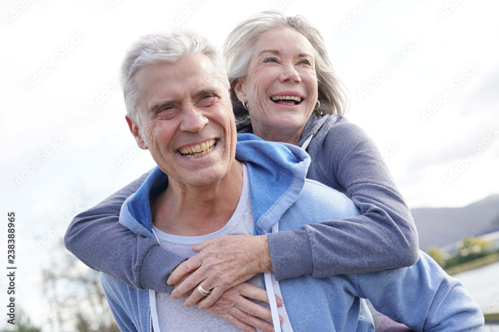 Fun loving senior couple piggyback riding outdoors Fun loving senior couple piggyback riding outdoors