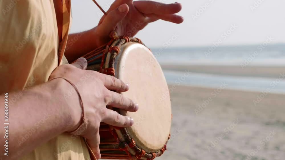 Man playing on a drum with his hands, close up. Hands tapping a small drum