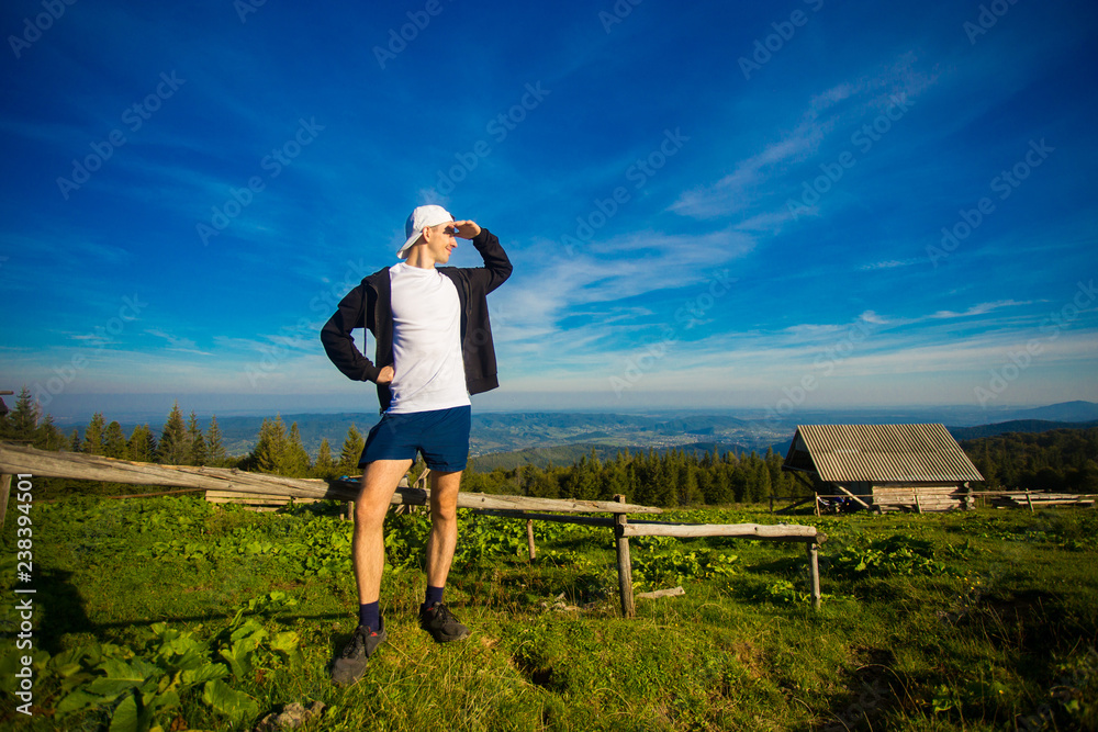 man hiker relaxing on top of hill and admiring beautiful mountain valley view in summer